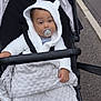 baby, black_stroller, blanket, casual, child, comfort, cozy, curious, cute, expression, hoodie, infant, outdoor, pacifier, pavement, small_hand, soft_texture, stroller, white_clothing, young_child