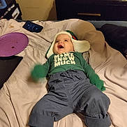 Daniel Moreno is registered to the contest to win money with this photo: baby, bed, blanket, child, clothing, cozy, green_mittens, happy, hat, indoor, infant, nightstand, pants, person, photograph, plush_toys, smile, socks, toy, warm_clothing