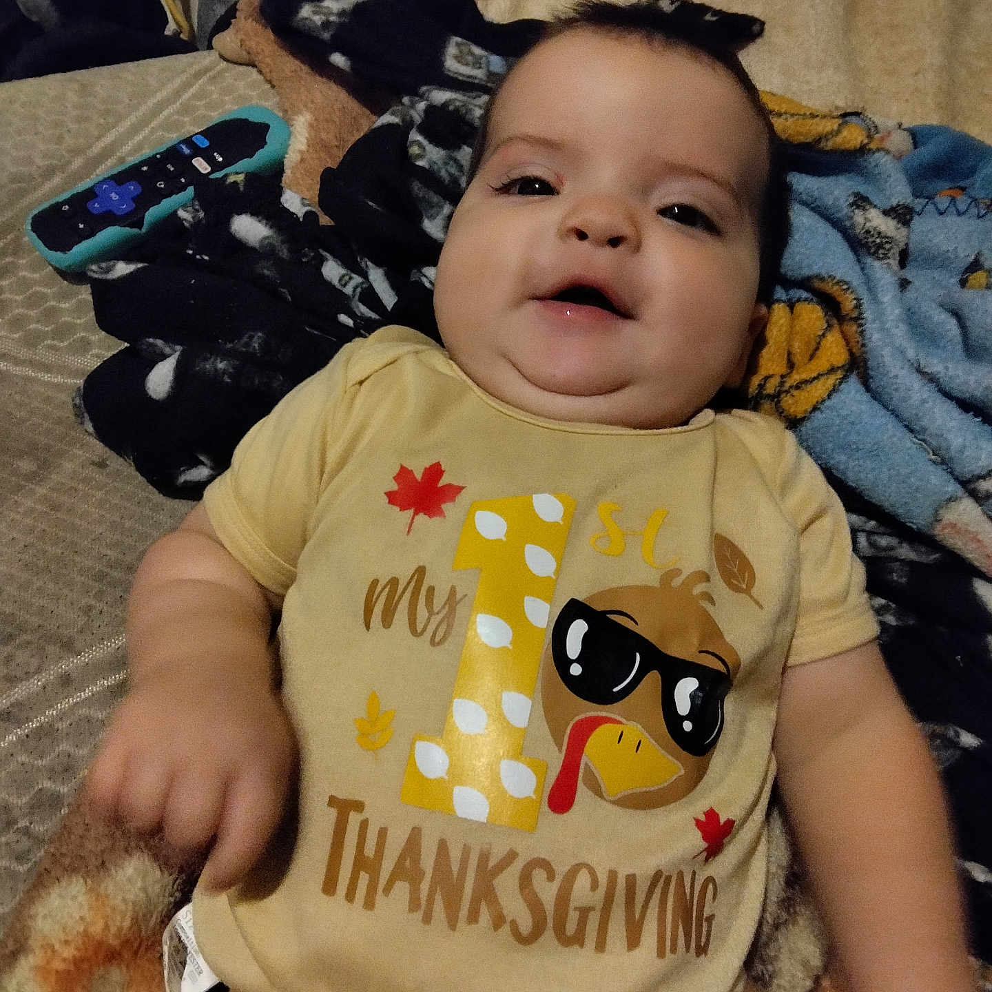 Daniel Moreno is registered to the contest to win money with this photo: baby, bed, blanket, cartoon, child, clothing, cozy, cute, face, happy, indoor, infant, lying_down, person, remote_control, shirt, smile, sunglasses, thanksgiving, turkey
