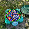 backyard, ball_pit, casual_clothing, child, colorful_balls, daylight, fun, grass, green_turtle, happy, nature, outdoor, plastic_balls, play, playtime, relaxing, sunlight, toddler, toy, young_child