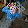 blue_pajamas, bookshelf, carpet, child, cute, face, floor, hand, headwear, indoor, paper_crown, person, playful, room, smiling, standing, superhero, toddler, toy, young_child