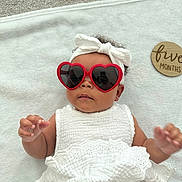 Kalani is registered to the contest to win money with this photo: baby, infant, sunglasses, heart_shaped, white_dress, headband, bow, blanket, five_months, cute, fashion, portrait, child, laying_down, accessory, adorable, person, baby_fashion, soft_texture, indoor
