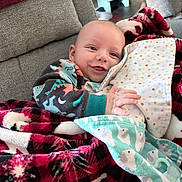 Jeremiah joined the competition — help win amazing prizes! baby, infant, smiling, blanket, plaid, dinosaur_onesie, clothing, couch, fabric, polka_dot, duck_pattern, hand, face, person, indoor, cozy, comfort, soft, pacifier, furniture