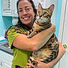 Cooper joined the competition — help win amazing prizes! woman, cat, bengal_cat, veterinary_clinic, green_scrub, smiling, indoor, holding, pet, animal, fur, face, eyes, hands, cabinet, sink, door, light_blue_wall, medical_posters, counter
