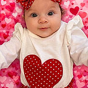 Amari is registered to the contest to win money with this photo: baby, infant, child, red_bow, polka_dot, heart_pattern, pink_background, white_shirt, cute, portrait, smiling, headband, clothing, fabric, sitting, face, eyes, adorable, closeup, baby_girl