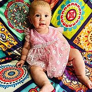 Aleigha is registered to the contest to win money with this photo: baby, child, pink_dress, floral_pattern, colorful_background, quilt, sitting, cute, portrait, indoors, happy, smiling, infant, face, legs, arm, patterned_fabric, bright_colors, person, young_child