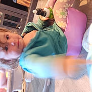 Atalli is registered to the contest to win money with this photo: baby, bottle, casual_clothing, child, curious, face, floor, floral_pattern, furniture, green_jacket, indoor, leggings, person, pink, play_area, potty, reaching_hand, toddler, wooden_floor, yellow_ball