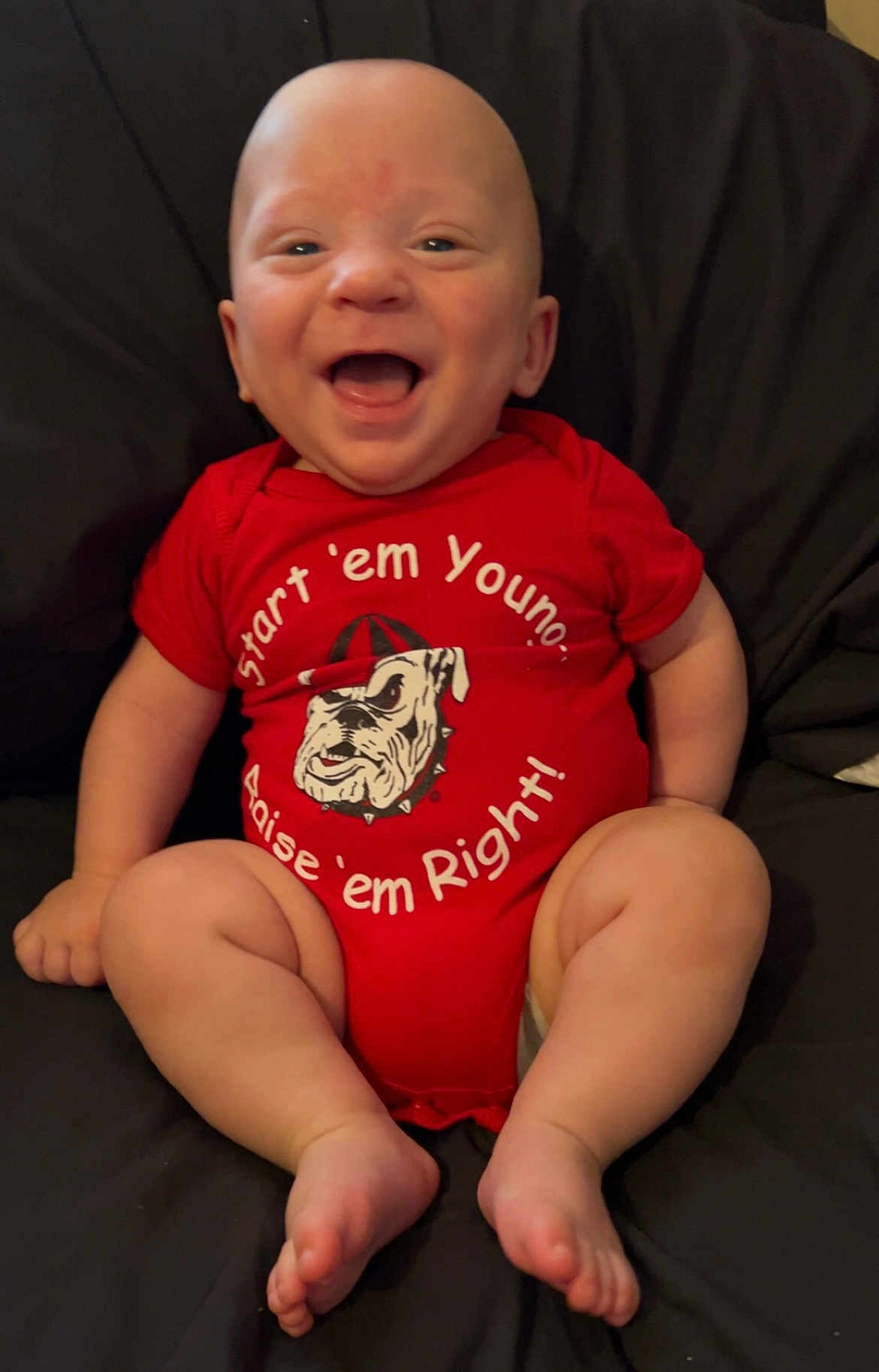 Austin joined the competition — help win amazing prizes! baby, infant, smiling, red_onesie, sitting, happy, face, barefoot, chubby_legs, cute, indoors, portrait, child, clothing, expression, skin, person, young, head, background