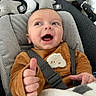 Elio a rejoint le concours — aidez-le/la à gagner de superbes lots ! baby, baby_seat, blanket, brown_clothing, child, closeup, comfort, cute, expression, face, happy, indoors, infant, infant_clothing, person, plush_toys, safety_harness, smile, stars, thumbs_up
