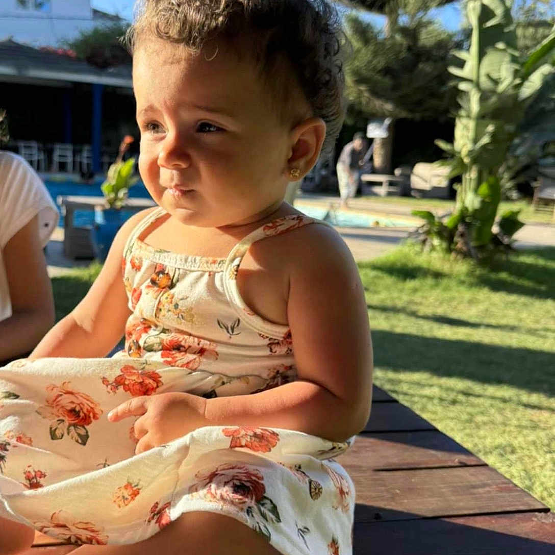 Zahraa a rejoint le concours — aidez-le/la à gagner de superbes lots ! child, curly_hair, daytime, dress, earrings, floral, grass, greenery, nature, outdoor, person, plant, portrait, sky, summer, sunlight, table, toddler, tree, wood