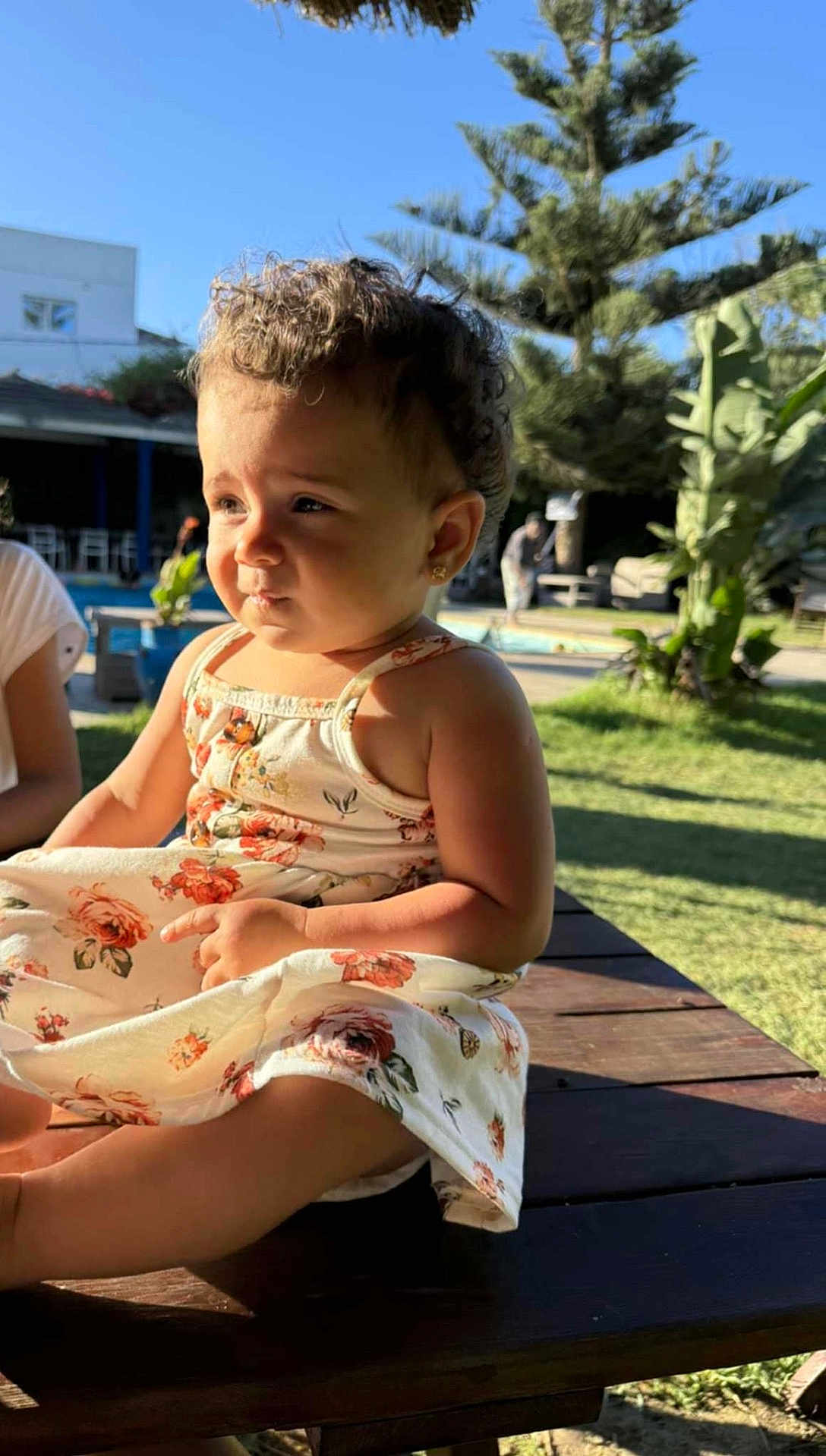 Zahraa a rejoint le concours — aidez-le/la à gagner de superbes lots ! toddler, child, outdoor, sunlight, dress, floral, table, wood, greenery, tree, plant, grass, sky, curly_hair, earrings, person, portrait, summer, nature, daytime