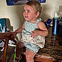 toddler, child, table, hand, romper, shoe, floor, chair, poster, water_bottle, kitchen, person, smile, blue_eyes, earring, indoor, holding_hands, marble_table, tile_floor, clothing