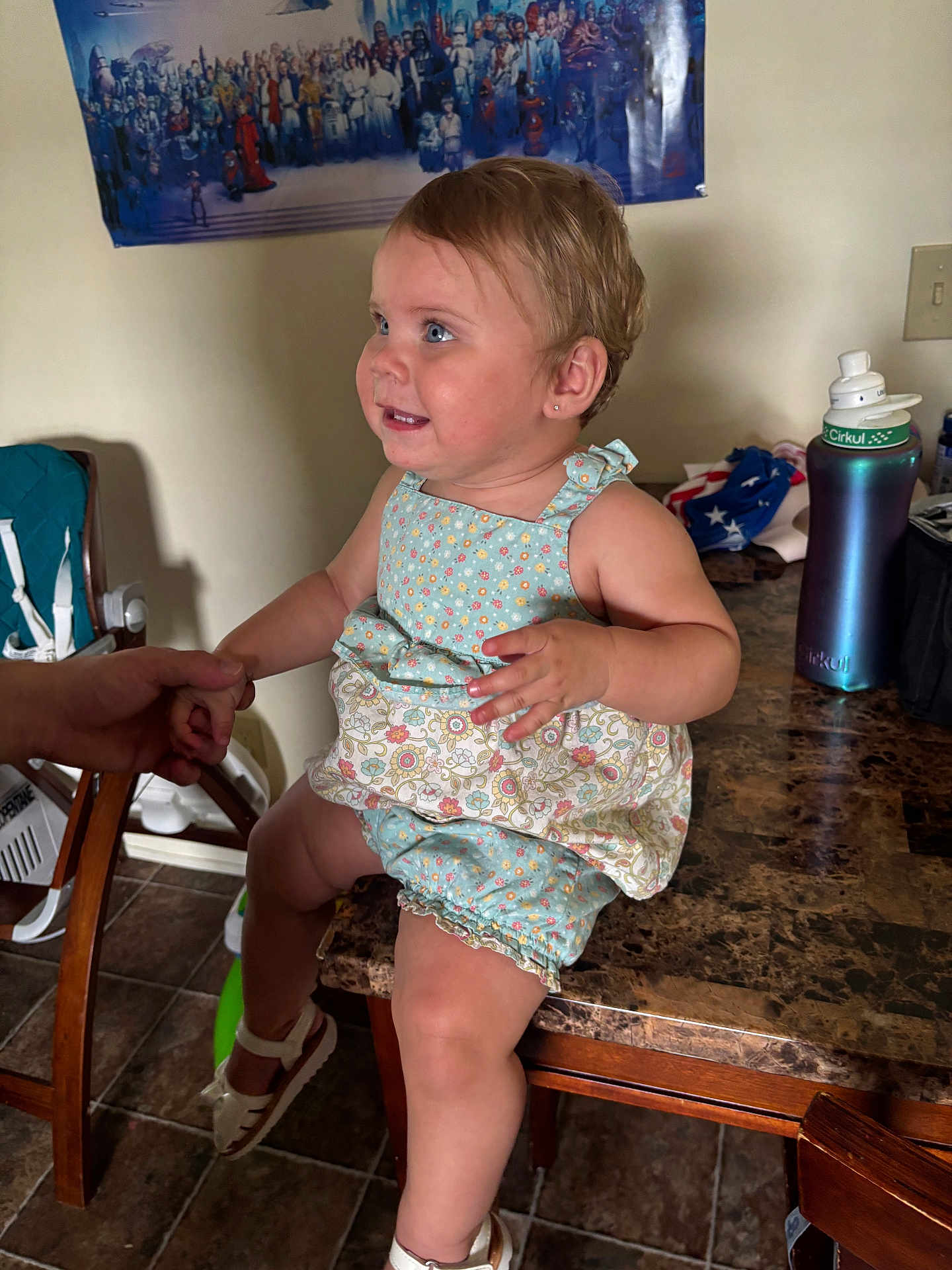 Leia is registered to the contest to win money with this photo: toddler, child, table, hand, romper, shoe, floor, chair, poster, water_bottle, kitchen, person, smile, blue_eyes, earring, indoor, holding_hands, marble_table, tile_floor, clothing
