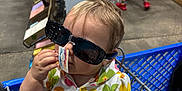 Leia joined the competition — help win amazing prizes! toddler, child, shopping_cart, sunglasses, price_tag, hand, adult_hand, store, aisle, boy, blue_jersey, plaid_shorts, red_shoes, floor, clothing, person, shopping, retail, indoor, casual
