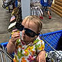 toddler, child, shopping_cart, sunglasses, price_tag, hand, adult_hand, store, aisle, boy, blue_jersey, plaid_shorts, red_shoes, floor, clothing, person, shopping, retail, indoor, casual