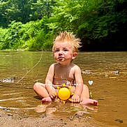 Samuel is registered to the contest to win money with this photo: toddler, child, water, river, nature, outdoor, summer, sunny, hair, spiky_hair, greenery, forest, sand, reflection, barefoot, cute, sitting, playful, emoji, sun