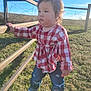 toddler, child, outdoor, grass, fence, sunlight, blue_sky, jeans, shirt, plaid, standing, holding, nature, casual_clothing, young_child, daylight, field, person, cute, walking