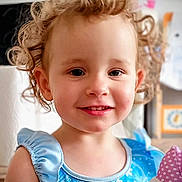 Aïna participe au concours pour gagner de l'argent avec cette photo : child, toddler, smiling, curly_hair, blue_dress, snowflake_pattern, plush_toy, indoor, portrait, cute, happy, young_child, face, person, holding, soft_toy, colorful, casual_clothing, closeup, bright