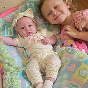 Paisley is registered to the contest to win money with this photo: baby, toddler, child, blanket, smile, indoor, floor, headband, clothing, patterned_pants, socks, curly_hair, wooden_floor, baby_bouncer, happy, cute, family, portrait, playtime, cozy