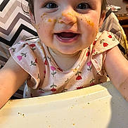 Elizabeth joined the competition — help win amazing prizes! baby, child, high_chair, messy_face, food, smiling, happy, indoor, cute, clothing, table, feeding, face, person, toddler, meal, expression, cheerful, pink, patterned_clothing