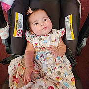 Sofia is registered to the contest to win money with this photo: baby, child, car_seat, dress, patterned_clothing, animal_print, plush_toy, unicorn, infant, cute, bow, sitting, indoors, person, face, hand, foot, happy, car_seat_warning_label, colorful