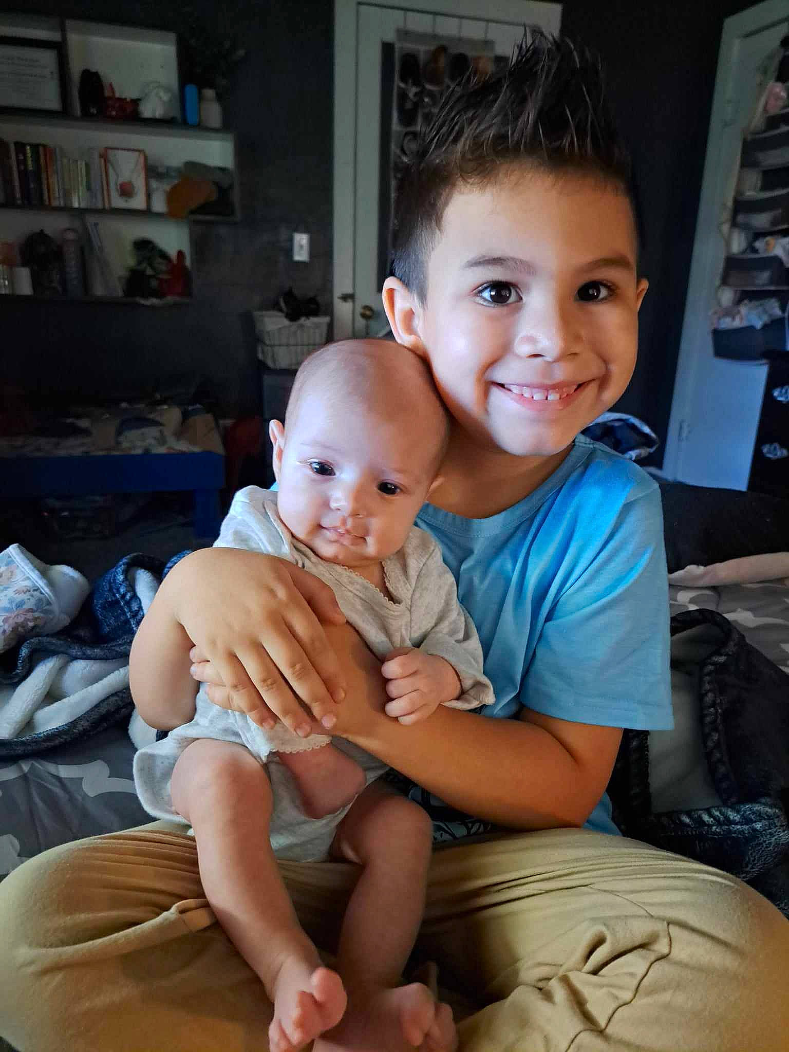 Hendrix is registered to the contest to win money with this photo: baby, bookcase, child, comfort, eye, fun, hairstyle, happy, human_leg, joy, lap, muscle, person, shelf, shorts, shoulder, sitting, skin, smile, thigh