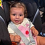 baby, child, car_seat, safety_harness, smiling, curly_hair, pink_shorts, white_shirt, indoor, seatbelt, cute, happy, infant, person, portrait, secure, young_child, bright, close_up, adorable