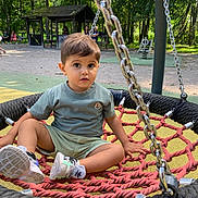 Youyou participe au concours pour gagner de l'argent avec cette photo : child, toddler, swing, playground, outdoor, trees, rope, seat, park, greenery, casual_clothing, shorts, tshirt, sneakers, daylight, people_in_background, bench, recreation, nature, curious_expression