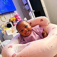 Dream is registered to the contest to win money with this photo: baby, bear_pattern, child, cute, decor, face, furniture, head, home, indoors, infant, inflatable_chair, joyful, pink, playful, purple_clothing, room, seated, smile, tongue_out