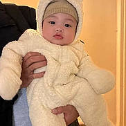 Nyler Wayne David joined the competition — help win amazing prizes! baby, child, infant, portrait, face, person, held, costume, bear_hood, winter_clothing, fluffy, white_outfit, hat, indoors, warm_lighting, doorway, chair, adult_hand, sitting, cute