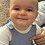 baby, child, smile, face, blue_overalls, white_shirt, wooden_buttons, hand, carpet, blanket, indoor, portrait, cute, happy, infant, person, closeup, skin, head, eyes