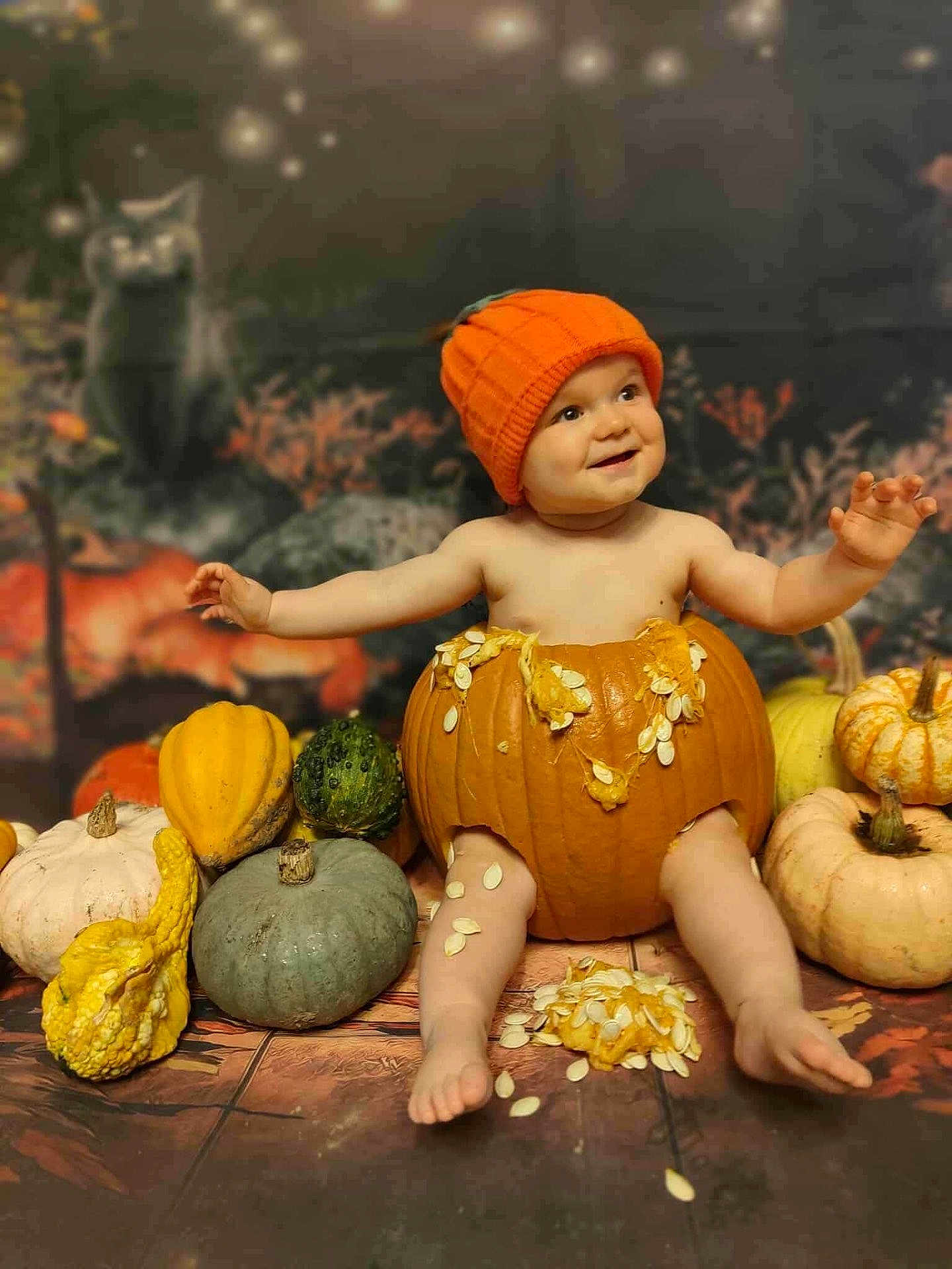 Riley is registered to the contest to win money with this photo: baby, pumpkin, orange_hat, gourds, fall, autumn, festive, smiling, child, cute, seed, floor, decor, holiday, background, sitting, happy, seasonal, cozy, portrait