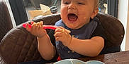 Riley is registered to the contest to win money with this photo: baby, high_chair, spoon, food, messy, plate, bread, table, window, glass_door, garden, car, plant, indoor, child, happy, smiling, feeding, blue_plate, red_spoon