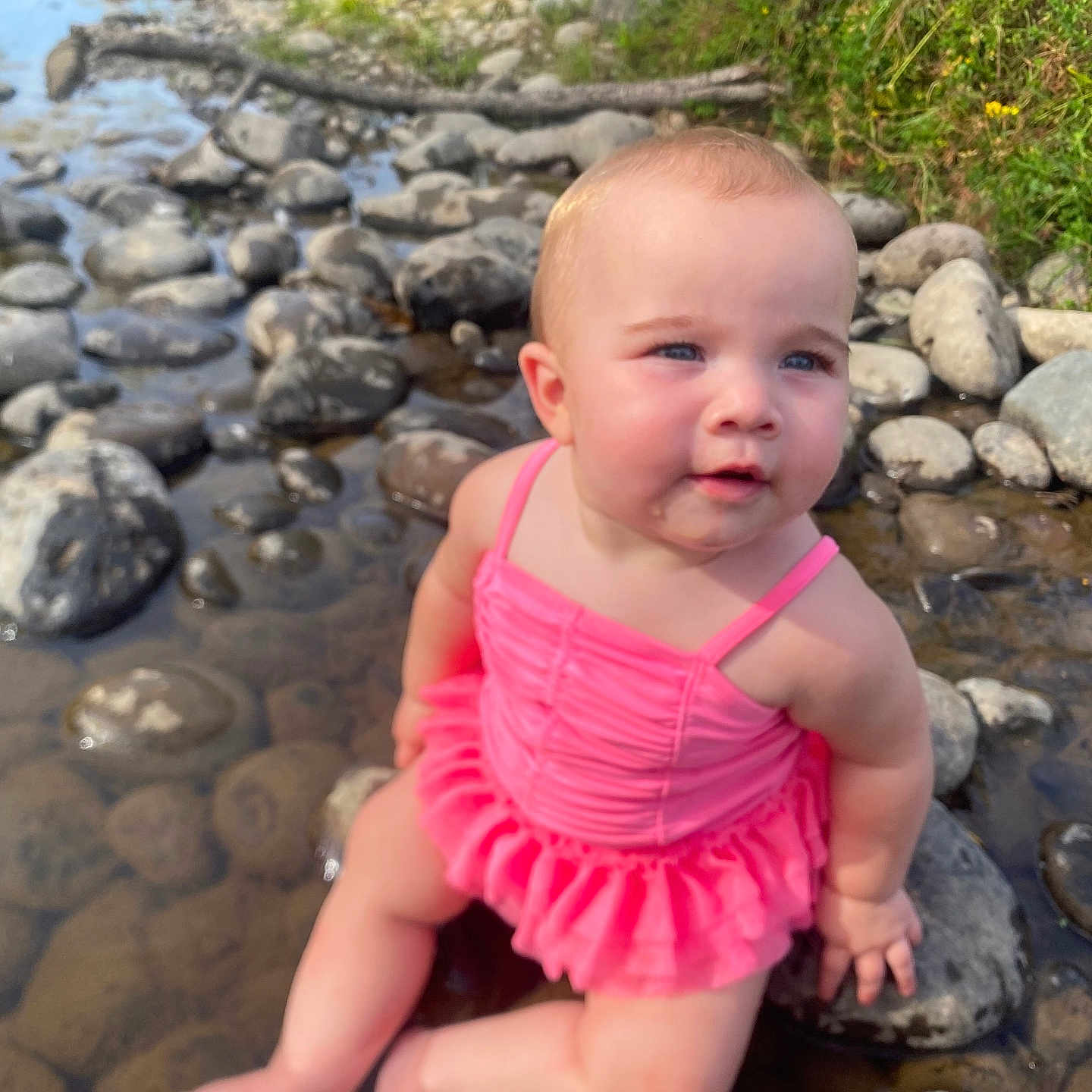 Ava joined the competition — help win amazing prizes! baby, child, pink_swimsuit, water, rocks, river, outdoor, nature, grass, sunlight, skin, barefoot, summer, portrait, sitting, cute, curious, blue_eyes, natural_light, stream