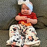 baby, child, smile, headband, red_shirt, cow_print_pants, barefoot, couch, gray_couch, seated, happy, cute, indoors, infant, clothing, person, portrait, hands, feet, home