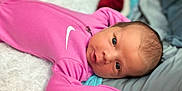 Oaklynn is registered to the contest to win money with this photo: baby, newborn, infant, pink_onesie, nike_logo, blanket, soft_texture, lying_down, close_up, face, eyes, curious, indoors, sleepwear, baby_clothing, portrait, head, skin, young_child, cute