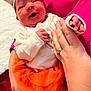 Oaklynn joined the competition — help win amazing prizes! baby, newborn, infant, child, headband, bow, orange_skirt, white_top, hand, adult_hand, manicure, rings, smile, happy, indoor, blanket, fabric, person, holding, cute