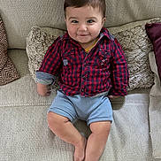 Kyle a rejoint le concours — aidez-le/la à gagner de superbes lots ! baby, child, smiling, couch, pillow, shirt, shorts, indoor, person, cute, happy, relaxed, home, infant, seated, plaid, barefoot, young, portrait, cozy