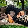 blanket, casual_clothing, companion, cozy, cushion, daylight, dog, fur, grass, nature, outdoor, peaceful, pet, pillow, relaxation, resting, sleeping, small_dog, tree, woman
