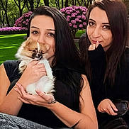 Bella is registered to the contest to win money with this photo: woman, dog, pomeraian, pet, outdoor, garden, flower, greenery, grass, portrait, black_clothing, long_hair, smile, cute, holding, friendship, nature, happy, casual, relaxation