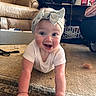 baby, crawling, smile, headband, bow, carpet, living_room, couch, furniture, curtains, bottle, toy, person, child, indoor, clothing, happy, floor, hand, face
