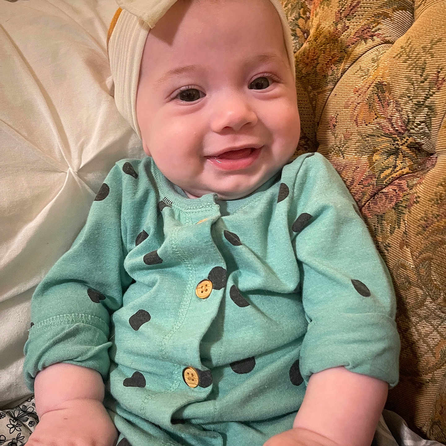 Lydia Faye Anne is registered to the contest to win money with this photo: baby, child, clothing, couch, cozy, cute, fabric, face, hand, happy, headband, indoor, infant, onesie, person, pillow, polka_dots, portrait, sitting, smiling