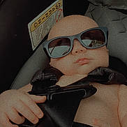 Jansen is registered to the contest to win money with this photo: baby, sunglasses, car_seat, seatbelt, infant, child, hand, face, head, clothing, safety, closeup, portrait, summer, accessory, cute, cool, seat, protection, resting