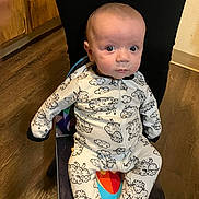 Jansen joined the competition — help win amazing prizes! baby, child, onesie, sheep_pattern, chair, wooden_floor, person, indoor, footwear, sitting, curious, wide_eyes, infant, cute, sleepwear, colorful, black_pants, flooring, young_child, portrait