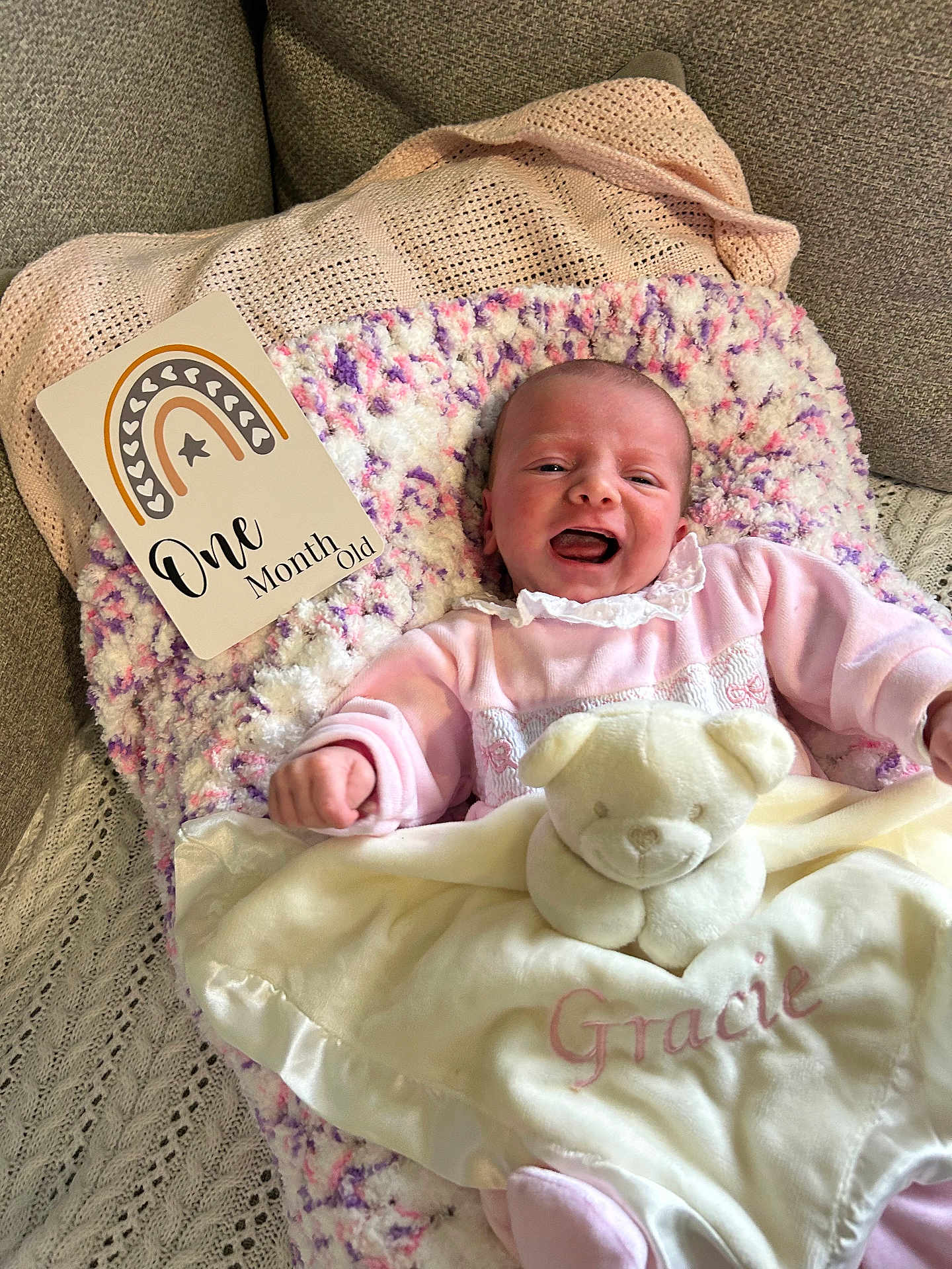 Gracie is registered to the contest to win money with this photo: baby, infant, smiling, blanket, teddy_bear, pink_clothing, couch, cozy, child, cute, portrait, one_month_old, happy, soft_toy, indoor, newborn, face, person, resting, comfort