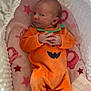 Gracie is registered to the contest to win money with this photo: baby, infant, orange_onesie, pumpkin_costume, blanket, pink_blanket, stars, elephant_pattern, white_cocoon, soft_texture, newborn, lying_down, cute, cozy, hands_clasped, curious_expression, indoors, sleepwear, footed_pajamas, portrait