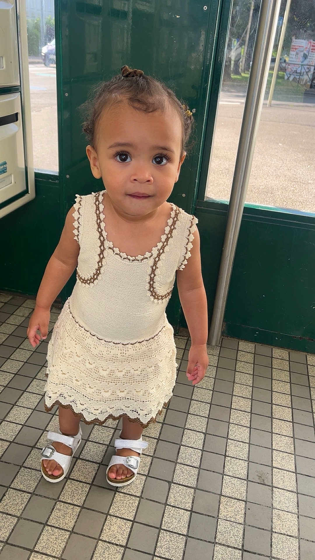 Kezia participe au concours pour gagner de l'argent avec cette photo : toddler, child, dress, sandals, standing, floor, tiles, indoors, door, green, window, natural_light, curly_hair, cute, person, young_child, portrait, expression, clothing, footwear
