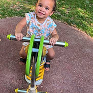 Kezia a rejoint le concours — aidez-le/la à gagner de superbes lots ! toddler, child, playground, spring_rocker, green, yellow, smiling, happy, outdoor, grass, pavement, summer, play, fun, cute, person, footwear, patterned_clothing, baby, park