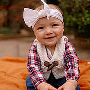 Brinley joined the competition — help win amazing prizes! baby, child, smiling, headband, bow, plaid, vest, jeans, shoes, blanket, outdoor, nature, greenery, blurred_background, happy, cute, portrait, sitting, toddler, hand