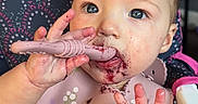 Brinley is registered to the contest to win money with this photo: baby, child, high_chair, bib, messy, berry_stains, purple, hand, face, blue_eyes, feeding, infant, cute, pink, clothing, sitting, indoor, expression, food, teething_toy